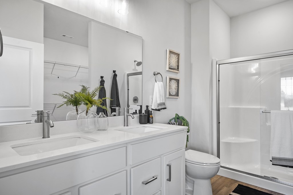 A white bathroom with a sink, mirror, toilet, and shower.