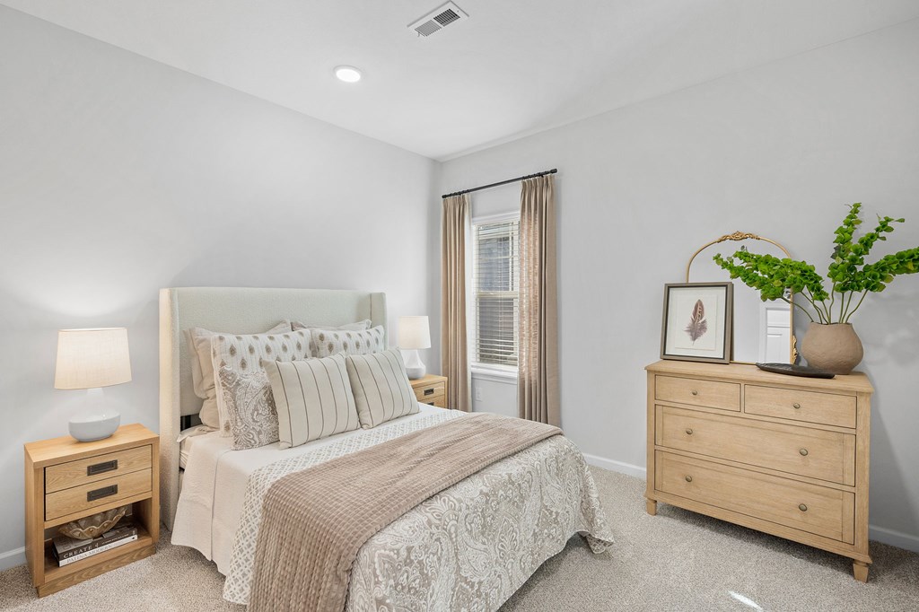 A bedroom with a bed, nightstand, and a plant on a dresser.