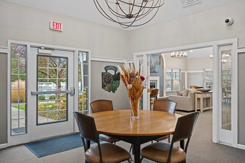 A dining room with a round table and chairs, a chandelier, and a view of the backyard through the glass doors.