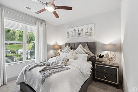 A bedroom with a large bed, a ceiling fan, and a window with blinds.