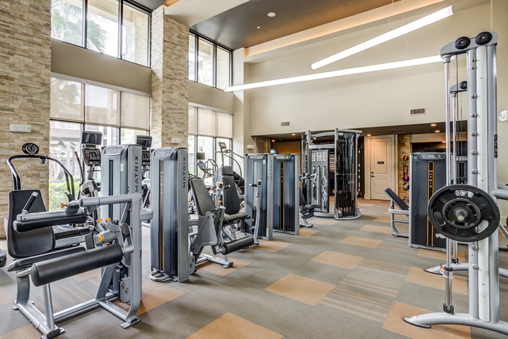 a fitness center with weights and cardio equipment in a building with windows