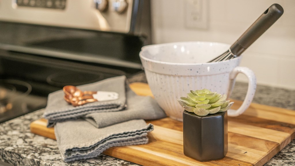 a cutting board with a cup and a plant on a kitchen counter