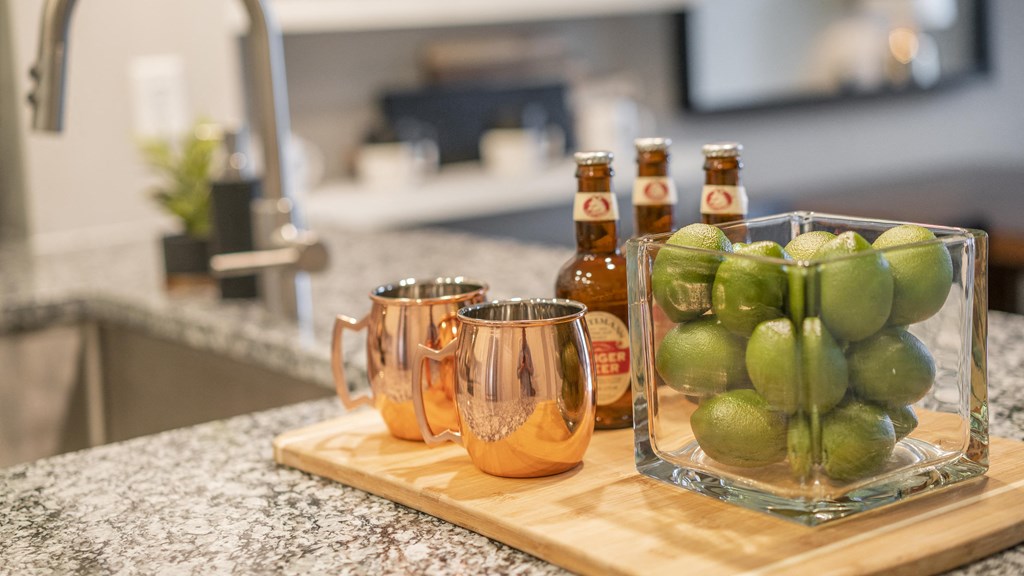 a cutting board with pitchers of apples and bottles of beer on a kitchen counter