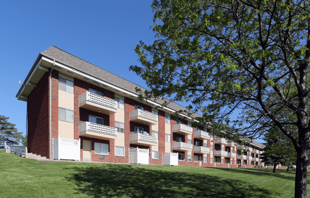 A red brick apartment building with a green tree in front.