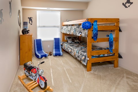A child's bedroom with a bunk bed, a chair, a toy motorcycle, and a window.