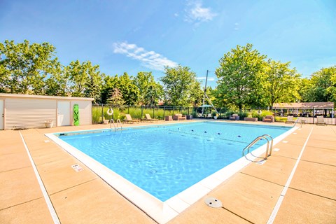 A large outdoor swimming pool surrounded by trees and a fence.