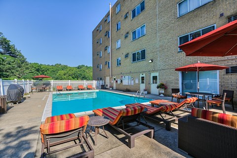 A pool area with chairs and umbrellas in front of a building.