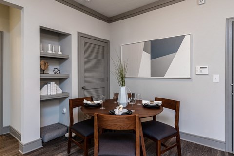 a dining area with a wooden table and chairs and a wall shelf