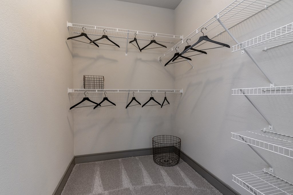 a walk in closet with white closets and racks and a basket on the floor