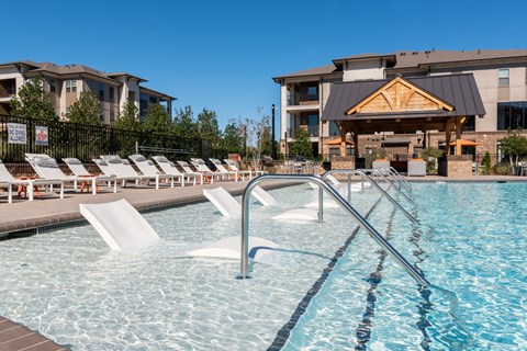 a swimming pool with chairs and a building in the background