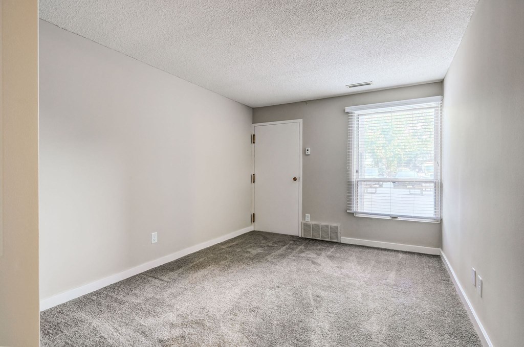 an empty living room with a window and carpet