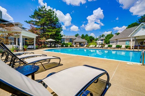 A pool surrounded by lounge chairs and umbrellas with houses in the background.