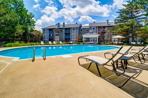 A large swimming pool with lounge chairs and a building in the background.