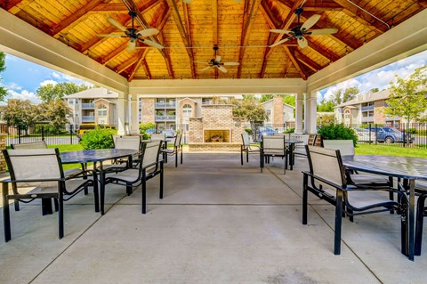 A patio with a table and chairs under a wooden roof.