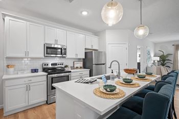 an open kitchen and dining area with white cabinets and stainless steel appliances