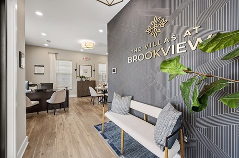 A living room with a couch and a plant in front of a wall with a sign that says "Villas at Brookview".
