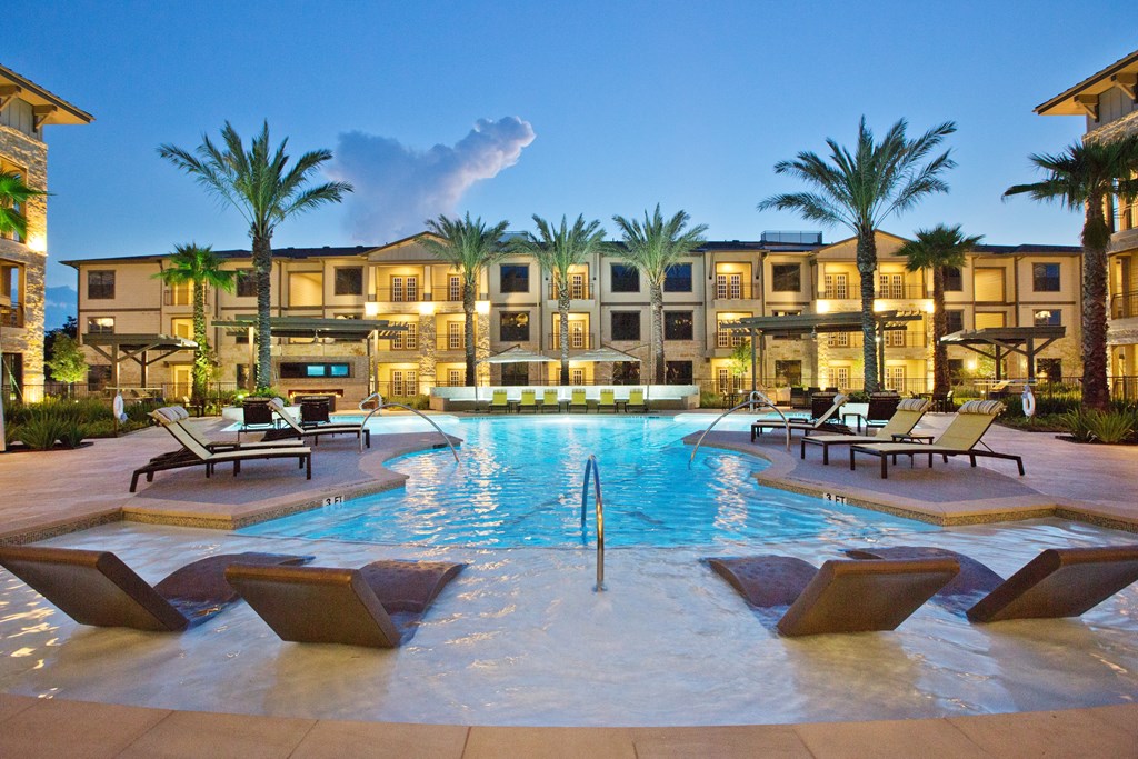 a large swimming pool with chairs in front of an apartment building