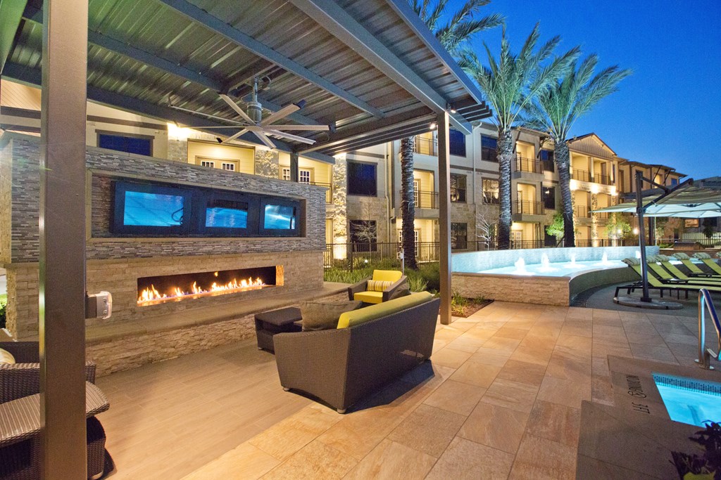 a patio with a fireplace and a pool at night