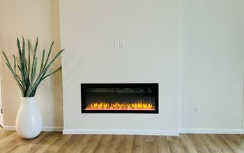 A white vase with green plants sits in front of a lit fireplace.