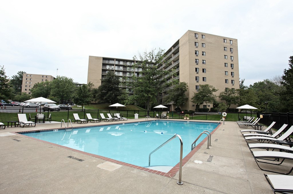 A large swimming pool surrounded by lounge chairs and umbrellas in front of a large building.