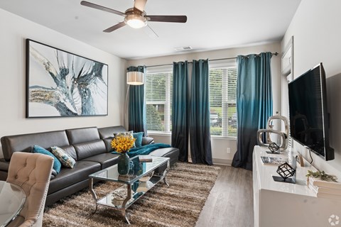 A modern living room with a black leather sofa, a glass coffee table, and a large painting on the wall.
