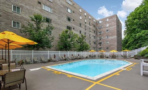 A swimming pool surrounded by a yellow fence and chairs with umbrellas.