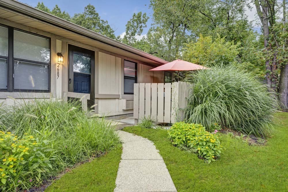 A house with a brown roof and a white fence with a garden in front.