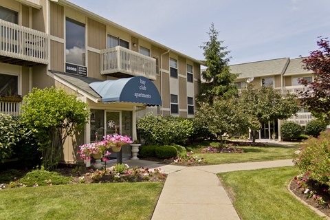A small building with a sign that says "hotel club apartments" is surrounded by a well-manicured lawn and garden.
