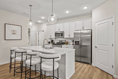 A kitchen with white cabinets and a white island with bar stools.