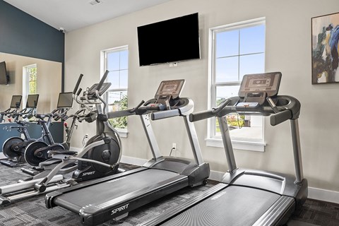 a gym with cardio machines and a tv on the wall