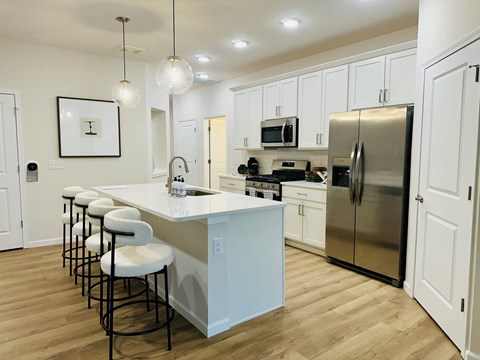 A kitchen with white cabinets and a white island with bar stools.