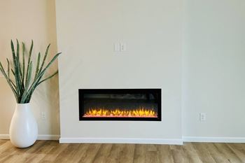 A white vase with a green plant sits next to a fireplace.