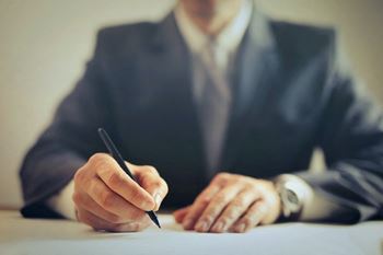 a man sitting at a desk signing a document with a pen