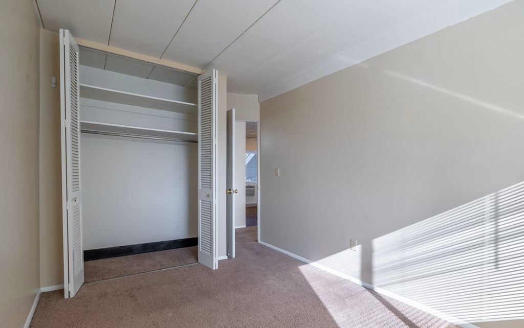 A room with a white wall and a white closet with shelves.