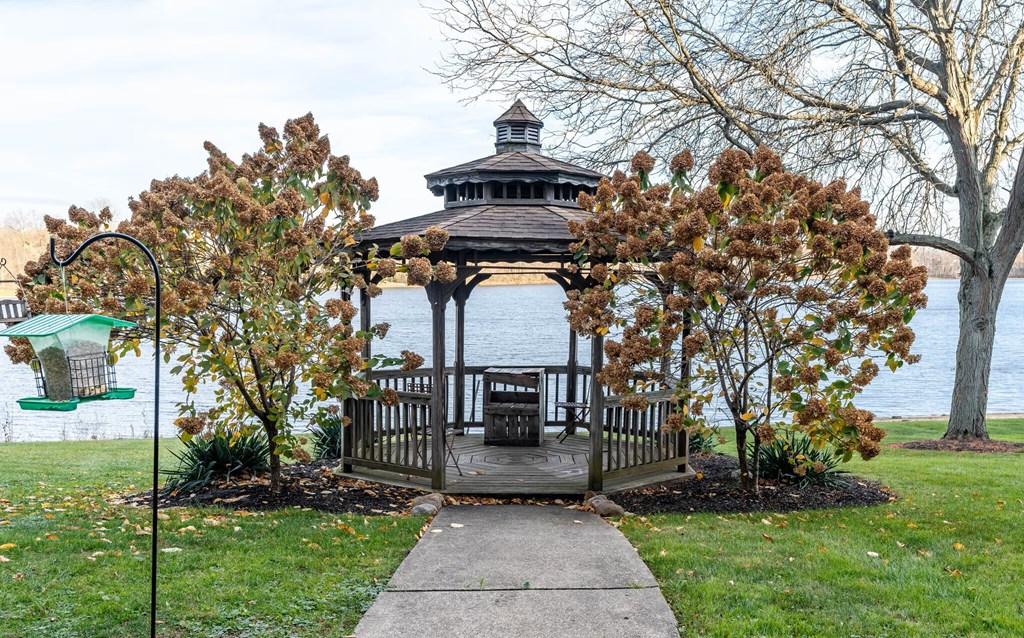 A gazebo is surrounded by trees and is located by a lake.