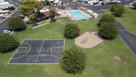 A basketball court is surrounded by a grassy area and a playground.