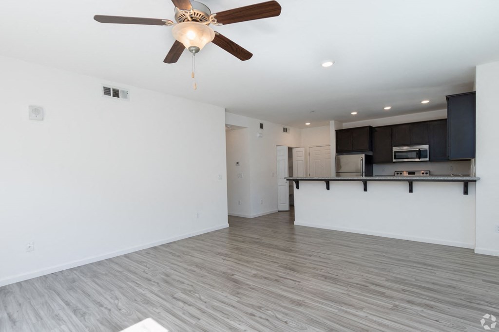 an empty living room with a ceiling fan and a kitchen