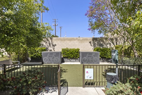 A sign with a bicycle symbol is attached to a fence in a green space.