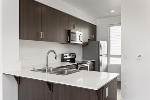 A modern kitchen with a white countertop and dark brown cabinets.