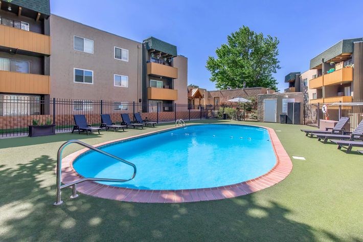 A swimming pool surrounded by a fence and chairs in front of apartment buildings.