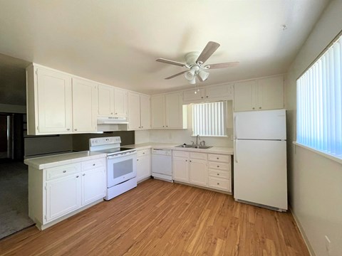 an empty kitchen with white appliances and a ceiling fan