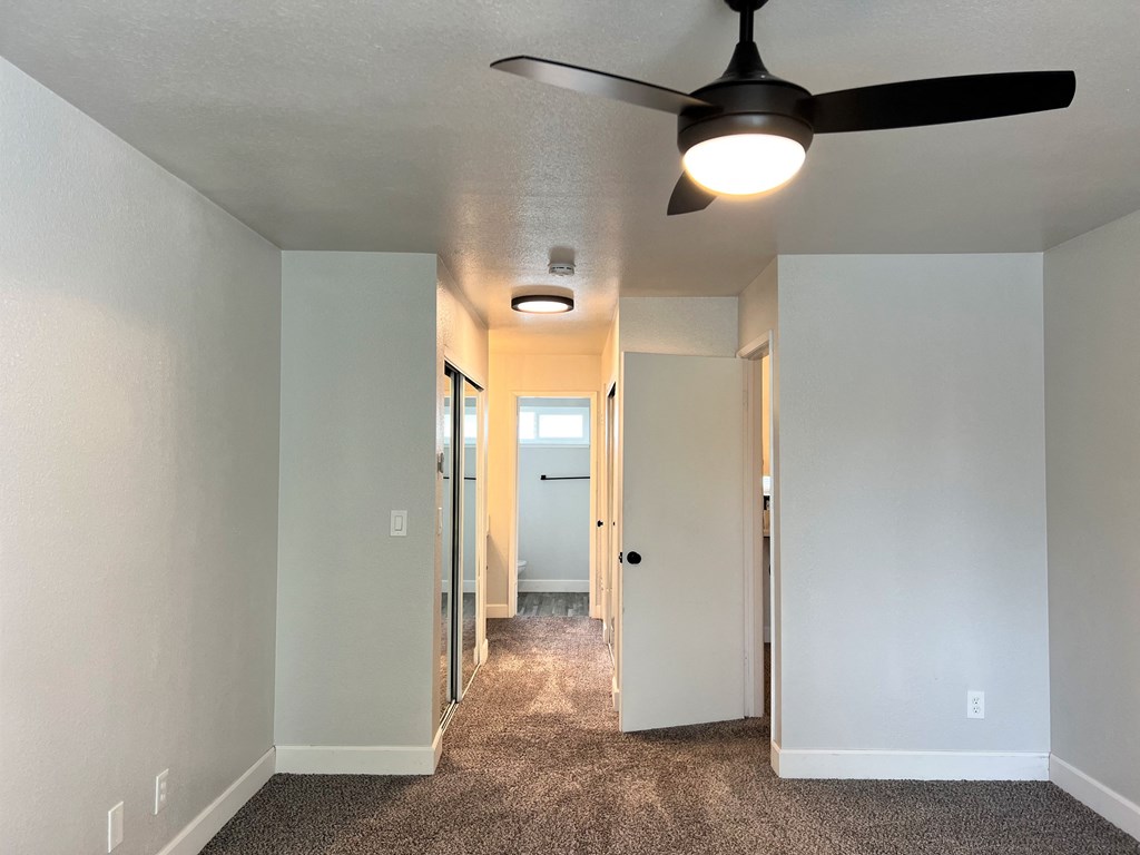 a bedroom with a ceiling fan and a hallway in the background