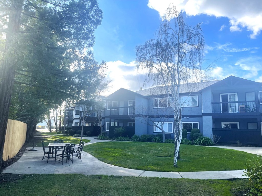 a yard with a table and chairs in front of an apartment building
