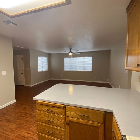 an empty kitchen with a white counter top and wooden floors