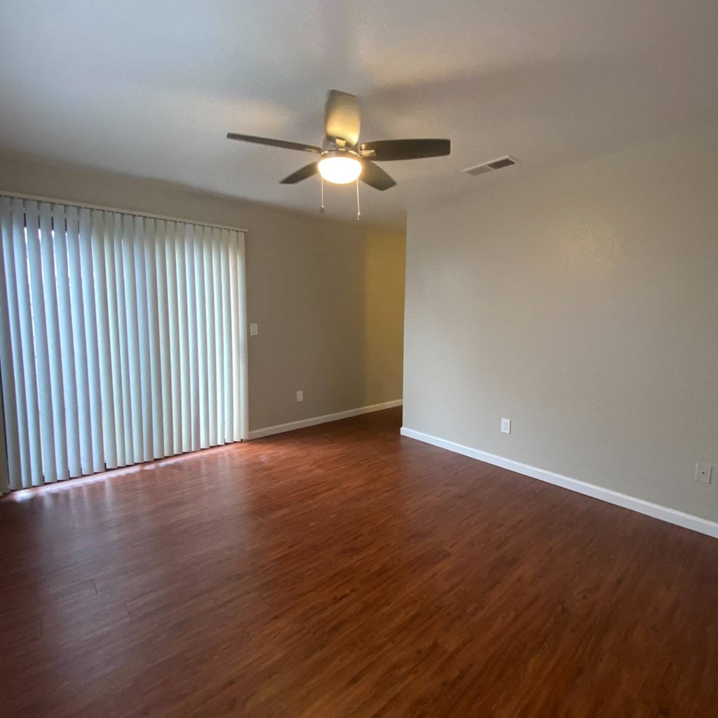 an empty living room with wood floors and a ceiling fan