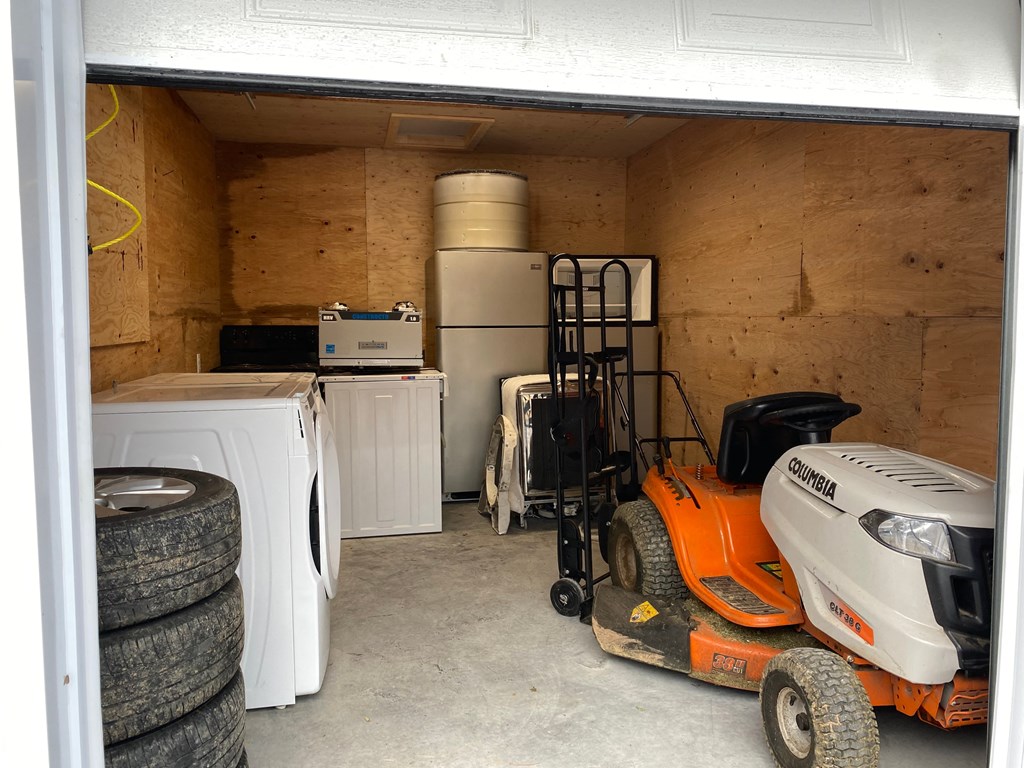 A storage space with a washing machine, a water heater, a vacuum cleaner, and a lawn mower.