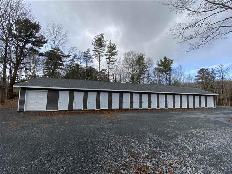 A long white building with a grey roof is surrounded by trees.