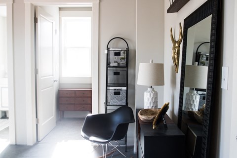 a corner of a room with a chair and a table with a lamp and a large mirror
