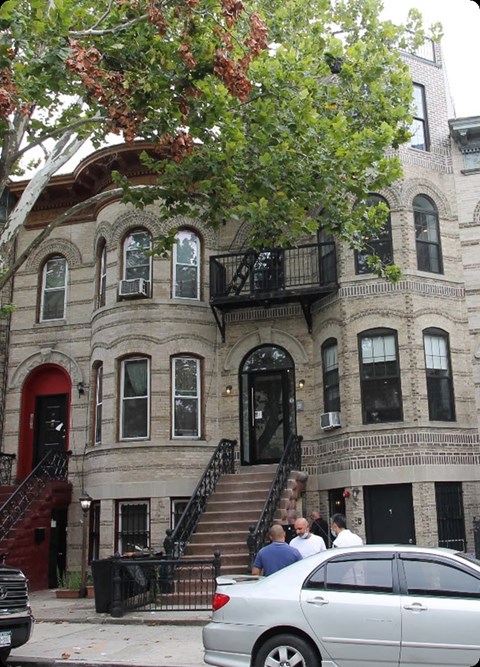 A silver car is parked on the street in front of a building with a red door.