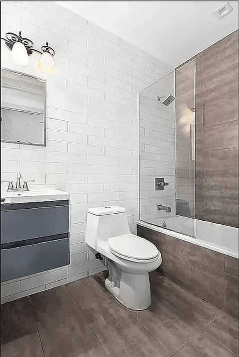 A white toilet sits in a bathroom with a white and brown tile wall.